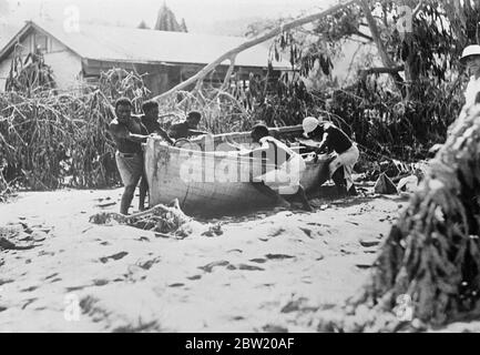 Erste Bilder von der Vulkankatastrophe auf der Insel Neuguinea. Drei Vulkane, zwei auf der Insel Vulcan und einer auf der Insel Matupi, brachen heftig unter Bimsstein und Schlamm auf den Dächern der Hauptstadt Rabaul der Insel Neubritanien in Neuguinea aus. Foto zeigt: Einheimische in Rabaul beim Abnehmen eines Bootes, das 300 Meter durch Flutwelle [Tsunami] an Land getragen wurde; gebrochene Bäume im Hintergrund. 18 Juni 1937 Stockfoto