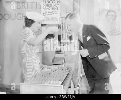 Besucher verkosten einen Probenaufropfen aus der Maschine bei der Bäckerausstellung in der Royal Agricultural Hall, Islington, London. Diese Maschine, die Donuts aus einer geheimen Formel nach Jahren der Forschung entwickelt macht, stellt sich heraus, 40 Dutzend der Backwaren in einer Stunde. September 1937. Stockfoto