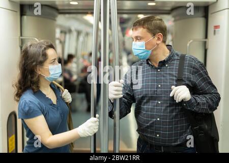 Mann und Frau tragen medizinische Einwegmasken und Gummihandschuhe freundlich reden, während der Fahrt mit der U-Bahn. Vorsichtsmaßnahmen während einer Coronavirus-Pandemie Stockfoto