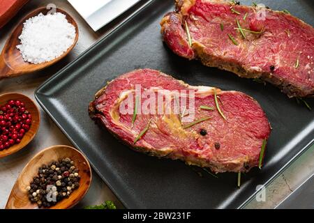 Marinierte rohe Steaks auf Steintisch mit Gewürzen Stockfoto