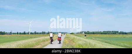 Frauen auf dem Fahrrad und Frühlingsblumen in der Nähe von Bereich mit Windkraftanlagen in der niederländischen Provinz flevoland Stockfoto