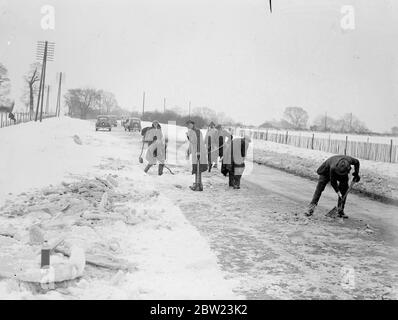 Ein 20-stündiger Schneesturm hat in Kent zu einer schweren Verrenkung geführt, wo Dörfer fast abgeschnitten wurden und Straßen durch Schneeverwehungen blockiert wurden, die in einigen Bezirken bis zu 8 Fuß tief sind. Viele Häuser sind komplett isoliert. Schneepflüge und Männerbanden mussten gestrandete Autofahrer zur Rettung bringen. Foto zeigt, Schnee von der Hauptstrasse Londons, Folkestone Road in Lenham zu räumen. 16 Februar 1938 Stockfoto