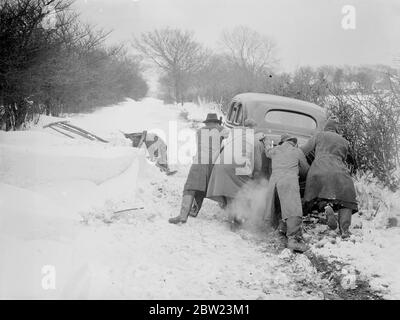 Schneesturm Haufen driftet 8 Fuß tief auf Kent Downs, Dörfer isoliert. Blizzard, der viele Stunden wütete, hat viele Meter tief dahindriftet und mehrere Kent-Dörfer mit Isolation bedroht. In einigen Fällen wurden Schneepflüge verwendet, um blockierte Straßen zu löschen. Zwischen Folkestone und Canterbury driftet auf den Höhen der Hecken auf den Downs mit Blick auf Folkestone, der Stil war 8 Meter tief. Foto zeigt, schiebt ein Auto aus einer tiefen Schneeverwehung in der Nähe des Dorfes Capel le Ferne, eines der Dörfer, die von Isolation bedroht sind. 16 Februar 1938 Stockfoto