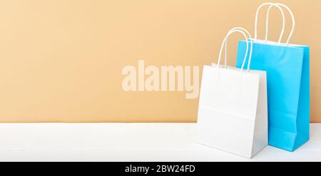 Weiße blaue Handarbeitspapiertaschen. Shopping Mockup Taschen Papier-Pakete auf weißem Tisch beige Licht Hintergrund mit Kopierraum. Einkaufen, Verkauf, Lieferung von Lebensmitteln Stockfoto