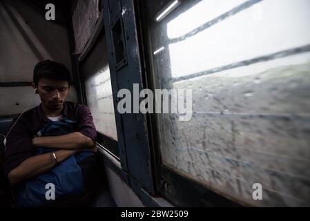 Mann, der aus dem Fenster des fahrenden Zuges der zweiten Klasse schaut. Indian Railways. Indien. Stockfoto