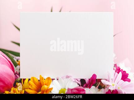 Blumen verspotten Glückwünsche. Glückwunschkarte in Blumenstrauß auf rosa Hintergrund. Weiße leere Karte mit Platz für Text, Frame Mockup Stockfoto