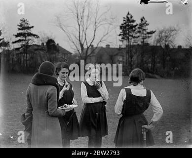 Eine Gruppe von Schülerinnen in Uniform essen Scheiben Zitrone mit einem Wince, Grimace, während auf dem Feld spielen Damen Hockey. 1933 Stockfoto