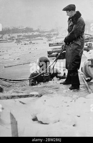 Tauchen unter dem Eis des Flusses Moskau. Obwohl der Moskauer Fluss dicht mit Eis bedeckt ist, wird die Arbeit der Verlegung von Abwasser- und Gasleitungen unter dem Flussbett von Tauchern weitergeführt. Die Arbeit, die von EPRON (The Soviet Ships Salvaging Trust) durchgeführt wird, ist für den Taucher sehr gefährlich. Wenn er durch irgendein Missgeschick von der Uferstation entfernt werden sollte, könnte er ohne Hoffnung auf Rettung ganz leicht Meilen unter dem Eis treiben. Aber die Shows, ein Taucher geht durch ein Loch im Eis des Flusses Moskau. Notieren Sie Eis auf der Rettungsleine. 12. Januar 1938 Stockfoto