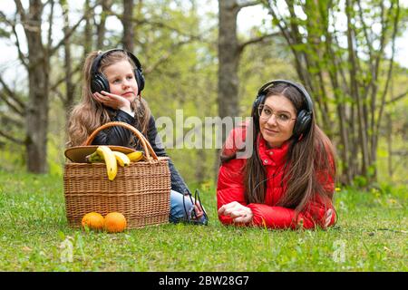An einem sonnigen Frühlingstag ruhen zwei Schwestern im Park neben dem Picknickkorb auf dem Gras und hören Musik, Konzept für Lifestyle und Freizeit Stockfoto