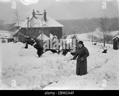Ihre Gärten in Hampshire aus dem Schnee graben. Die schlimmsten Schneestürme im Dezember seit vielen Jahren hatten Chaos nach Südengland gebracht, wo viele Dörfer durch Schneeverwehungen abgeschnitten worden waren. Autos wurden von ihren Fahrern verlassen und auf den Straßen gelassen, um fast vom Schnee begraben zu werden. Foto zeigt eine Weihnachtskarte in der Nähe von Ringwood, Hampshire, wo ein Mädchen klar und tief Schnee aus dem Garten eines malerischen Häuschen ist. Dezember 1937 Stockfoto