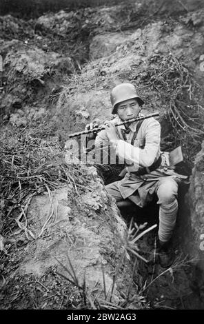 Musikalisches Zwischenspiel im China-Krieg. Ein chinesischer Stahlhelm Soldat, der anscheinend die Musik seiner Flotte für die Nerven beruhigend fand, als er in einem flachen Graben nahe Shanghai hockte. Vielleicht hoffte er, dass die seltsamen Noten helfen würden, die Japaner zu erschrecken!. 24. November 1937 Stockfoto