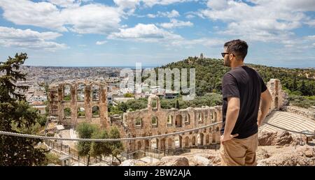 Herodes Atticus Odeon, Herodium, antikes Theater unter der Akropolis, Griechenland. Junger Mann, der die Stadt Athen über dem Theater betrachtet, sonniger Frühlingstag Stockfoto