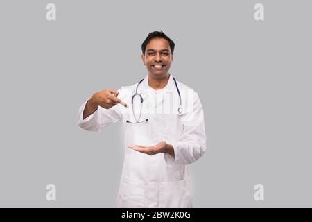 Arzt zeigt auf leere offene Hand vor der Brust isoliert. Indian Man Doctor Advertisment Konzept Stockfoto