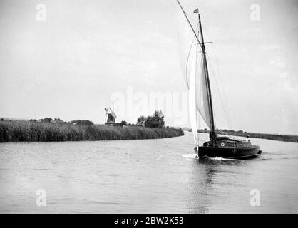 Die Broads, Norfolk. Wherry segelt auf einem Fluss / Kanal, eine Windmühle im Hintergrund 1934 Stockfoto
