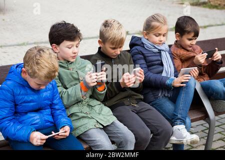 Gruppe von jugendlichen Kindern sitzt auf der Bank im Freien, in ihre Telefone süchtig Stockfoto