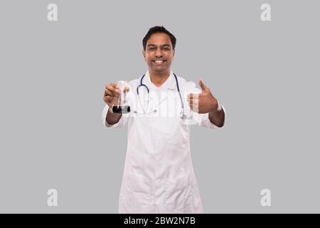 Männlich Arzt zeigt Flasche mit Colorfull Flüssigkeit und Daumen nach oben isoliert. Wissenschaft, Medizin, Virenkonzept. Indischer Mann Arzt Smilling. Stockfoto