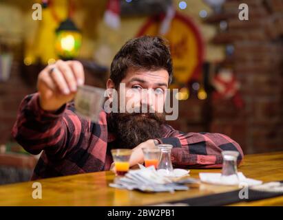 Hipster hält Geld, Bargeld, um mehr Alkohol zu kaufen. Mann mit betrunkenem Gesicht sitzt allein an der Theke. Kerl verbringen Freizeit in der Bar trinken Cocktail, entkokettes Hintergrund. Getränkekonzept bestellen. Stockfoto