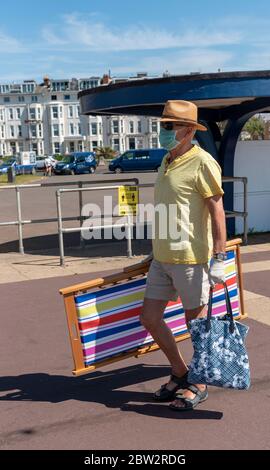 Southsea, Portsmouth, England, Großbritannien. Mai 2020. Mann, der während des Covid-19-Ausbruchs eine medizinische Maske und Handschuhe trägt, die einen Liegestuhl entlang der Promenade tragen. Stockfoto