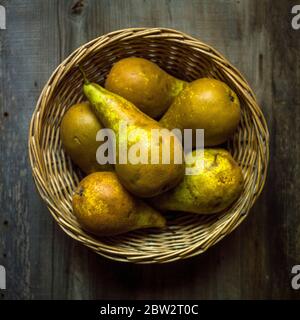 Ein Schuss frischer Birnen in einem Strohkorb auf einem Holztisch Stockfoto