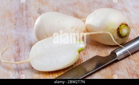 Nahaufnahme von ganzen und halbierten organischen weißen Radieschen auf Holzoberfläche. Gesunde vegetarische Zutat Stockfoto