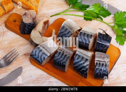 In Scheiben geschnittene ​​light gesalzene Makrele auf Holzschneidebrett mit frischem Baguette serviert. Fisch-Vorspeise Stockfoto