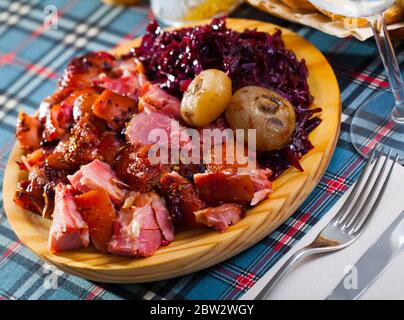 In Scheiben geschnitten gebackenes Schweinefleisch Schaft mit gemüsegarnitur von geschmorten Rotkohl auf Holzbrett serviert. Stockfoto