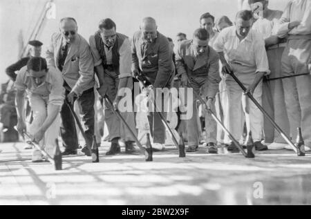 Spiele auf der Terrasse an Bord eines Ozeandampfers in den 1930er Jahren. Hier ist eine Variante des Spiels "Shuffleboard" mit einem Rennen, bei dem leere Bierflaschen von sechs männlichen Passagieren mit langen Stöcken mitgeschoben werden. Stockfoto