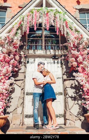 Gemischte Rennen paar in Liebe umarmen draußen. Arabischer Mann und weiße Frau, die durch die Stadt am Eingang des Cafés unter Blumen spazieren. Stockfoto