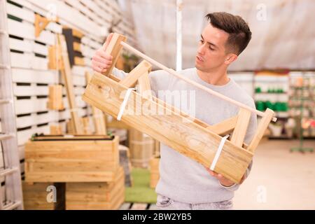 Junger Mann, der auf dem Gartenmarkt eigenartige Holzpflanzen für Blumen auswählt Stockfoto