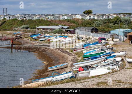 Eine große Anzahl von Booten, die von einer Werft am Chesil Strand mit einem Ferienpark im Hintergrund befahren werden Stockfoto