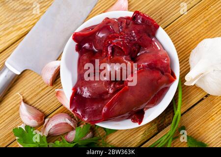 Frische rohe Kaninchenleber mit Gewürzen auf Holzgrund. Diätetisches Fleischprodukt Stockfoto