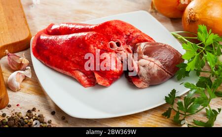 Zutaten zum Kochen. Rohe Hammellunge und Herz mit Zwiebel, Knoblauch, Gewürzen und Kräutern auf Holztisch Stockfoto