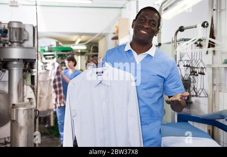 Fröhliche African American man Arbeiter der Dry Cleaner, saubere Kleidung nach chemische Reinigung Stockfoto