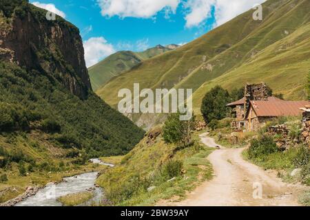 Eine unbefestigte Straße, die das Truso-Tal entlang des Flusses Tergi (Terek) führt, führte an einem alten Haus in der Region Kazbegi, Georgien Stockfoto