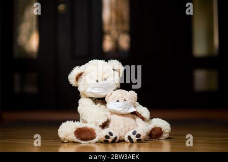 Zwei Teddybären in medizinischen Masken sitzen in der Nähe der Haustür im Flur des Hauses. Stockfoto