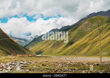 Blick auf das Mnaisistskali Flusstal in der Region Kazbegi, Georgien, während der Sommerzeit. Eine Stromleitung erstreckt sich über den Rahmen Stockfoto