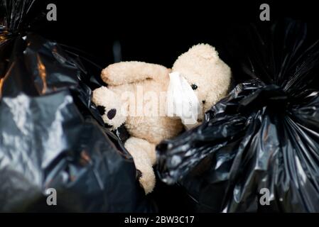 Ein Teddybär in einer medizinischen Maske liegt in der Kofferraum eines Autos auf Mülltüten Stockfoto