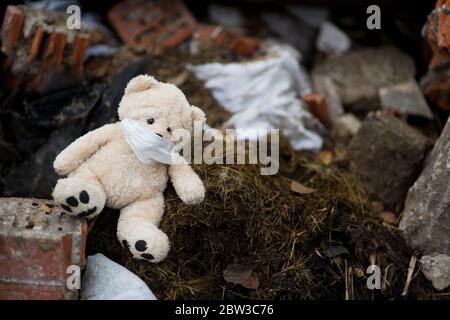 Ein ausgeworfene Teddybär in einer medizinischen Maske liegt auf Ein Haufen Müll Stockfoto