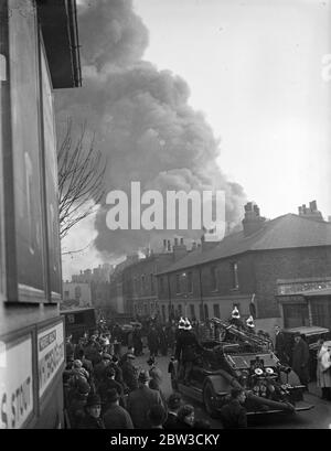 Eine riesige Rauchfasse hängt über den Häusern in Hammersmith, West London, als ein Feuerwehrmann die Straße hinauf geht, um mit dem Brand in einer Reifenfabrik umzugehen. 26. November 1934 Stockfoto