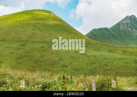 Ein grasbewachsener Hügel mit dem Wort "Gudauri", der von weiß bemalten Felsen auf der Spitze angeordnet ist, gegenüber dem Gudauri-Aussichtspunkt, Mzcheta-Mtianeti-Region, Georgien Stockfoto