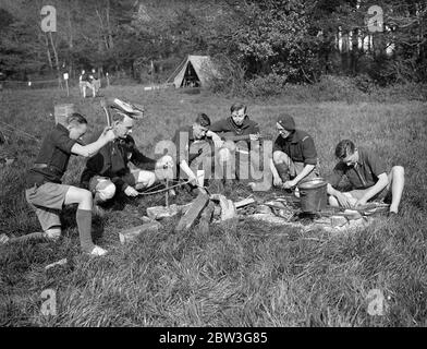 Beste Aufgabe des Tages . Orden der Holzhandwerk Ritterschaft Mitglieder in Sussex, Osterlager. Tragen die malerischen und malerischen Kostüme ihrer Organisation, Mitglieder des Ordens der Holzhandwerk-Chivalry, der Outdoor-Verein für Jugendliche und Mädchen gebildet, haben in Camp in der Nähe von Brighton für Osterferien gegangen. Mitglieder des Ordens sind alle Altersgruppen und kommen aus allen Grafschaften Englands ins Sussex-Lager. Foto zeigt, Einstellung der Kochhäuser Müdigkeit zu Musik im Sussex Camp. 11. April 1936 Stockfoto