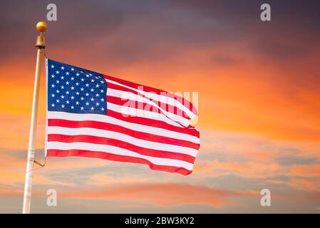 Amerikanische Feier- USA Flagge amerikanische Flagge auf Fahnenmast fliegen, über einem schönen und bunten Sonnenuntergang / Sonnenaufgang Himmel mit Wolken im Hintergrund Stockfoto