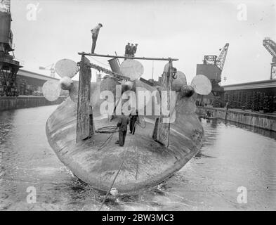 König Albert, einmal Stolz der deutschen Marine, wird in Rosyth gebrochen. Die Arbeit hat in Rosyth Dockyard, Schottland, auf die Auflösung der 20, 000 Tonnen Ex-deutschen Schlachtschiff König Albert, die von Scapa Fluss gerettet wurde, wo sie mit anderen deutschen Schiffen nach dem Krieg versenkt wurde begonnen. Der Hulk, der auf dem Kopf liegt, wird nach oben geschorben, damit das Wasser aus dem Dock herauslaufen kann. Foto zeigt, Arbeiter unter den massiven Propeller des König Albert beschäftigt, wie sie die Ausrüstung demontieren. 25 Mai 1936 Stockfoto