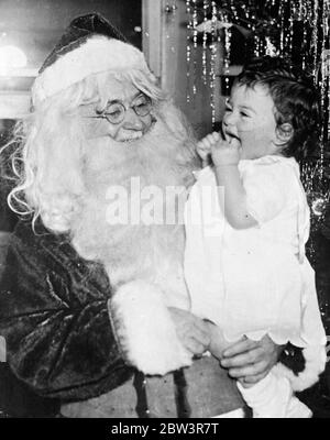 Exklusive Bilder der Dionne Quintuplets Weihnachtsfeier. Emelie, jubelnd über ihren Weihnachtsbaum und Spielzeug, lacht aufgeregt in den Armen von Pater Weihnachten Dr. Dafoe. 23 Dezember 1935 Stockfoto