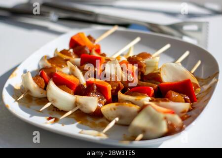 Marinierte rohe Hähnchenspieße auf Holzspieße mit Paprika und Zwiebeln in einer Satay-Marinade auf einem Teller draußen an sonnigen Tag in der Sonne. Stockfoto
