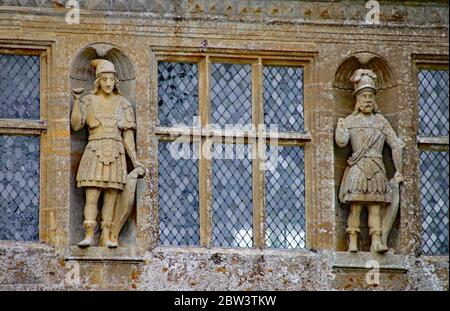 Zwei geschnitzte Figuren stehen auf beiden Seiten der Bleifenster in einem englischen Landhaus in Somerset Stockfoto