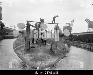 König Albert, einmal Stolz der deutschen Marine, wird in Rosyth gebrochen. Die Arbeit hat in Rosyth Dockyard, Schottland, auf die Auflösung der 20, 000 Tonnen Ex-deutschen Schlachtschiff König Albert, die von Scapa Fluss gerettet wurde, wo sie mit anderen deutschen Schiffen nach dem Krieg versenkt wurde begonnen. Der Hulk, der auf dem Kopf liegt, wird nach oben geschorben, damit das Wasser aus dem Dock herauslaufen kann. Foto zeigt, Arbeiter unter den massiven Propeller des König Albert beschäftigt, wie sie die Ausrüstung demontieren. 25 Mai 1936 Stockfoto