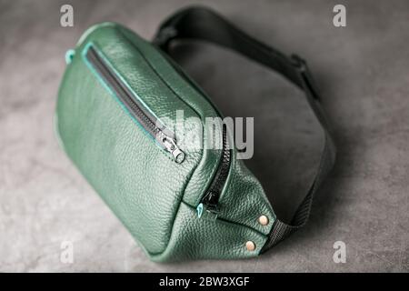 Gürteltasche aus dunkelgrünem Strukturleder, Banane auf grauem Hintergrund. Stockfoto