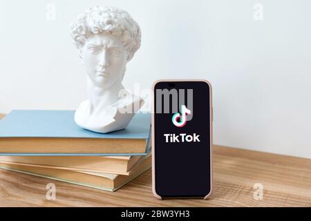 Kiew, Ukraine - 28. Mai 2020: TikTok-Anwendungslogo auf iPhone X-Bildschirm auf Holztisch mit Büchern und David-Kopf-Statue. TikTok ist ein Video-Sharing Stockfoto