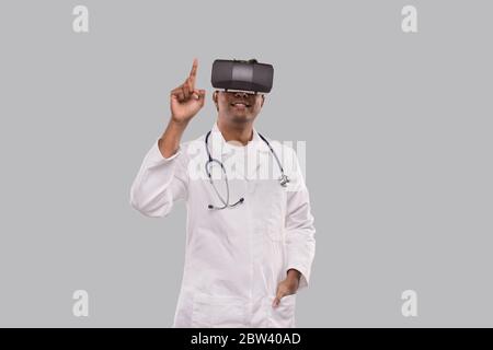 Arzt trägt VR-Brille klopft isoliert. Indischer Mann Arzt zeigt in virtuelle Realität Stockfoto